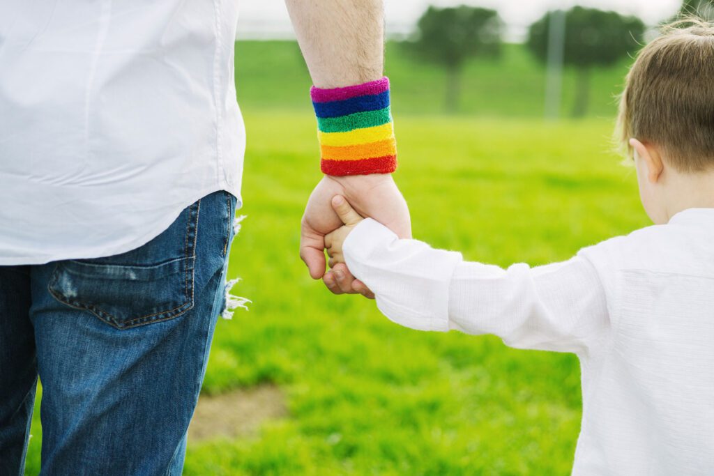 adult with rainbow wristband holds child's hand