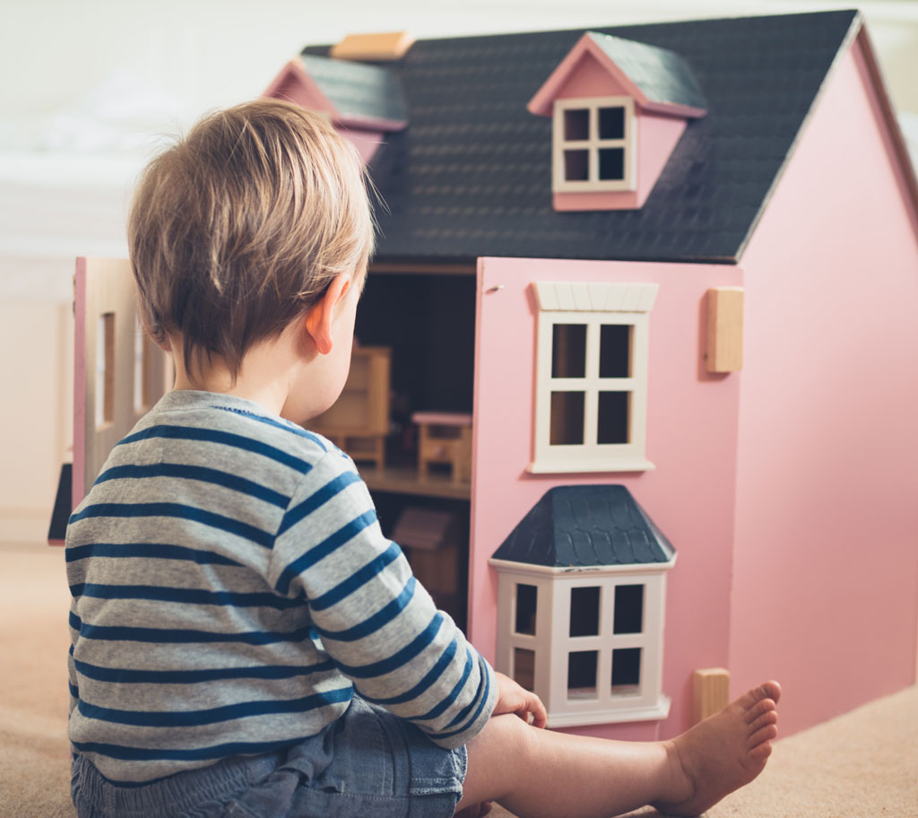 child sitting next to dollhouse