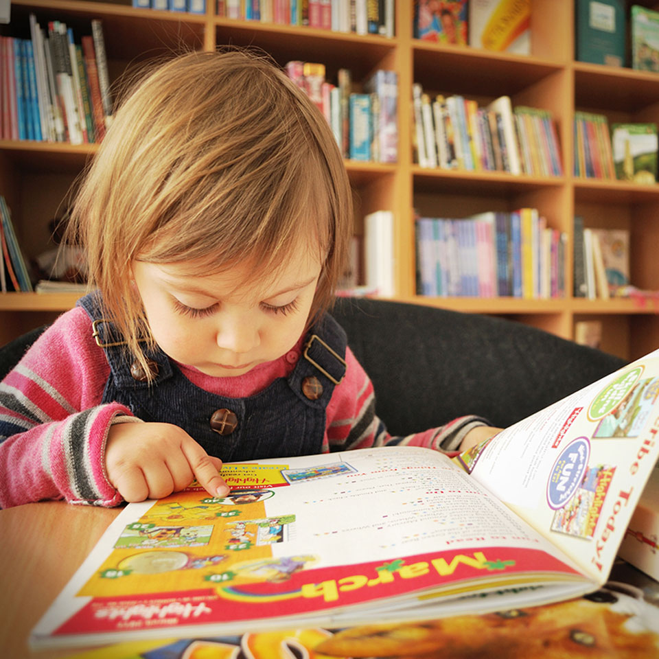 child reading book at table in front of bookshelves