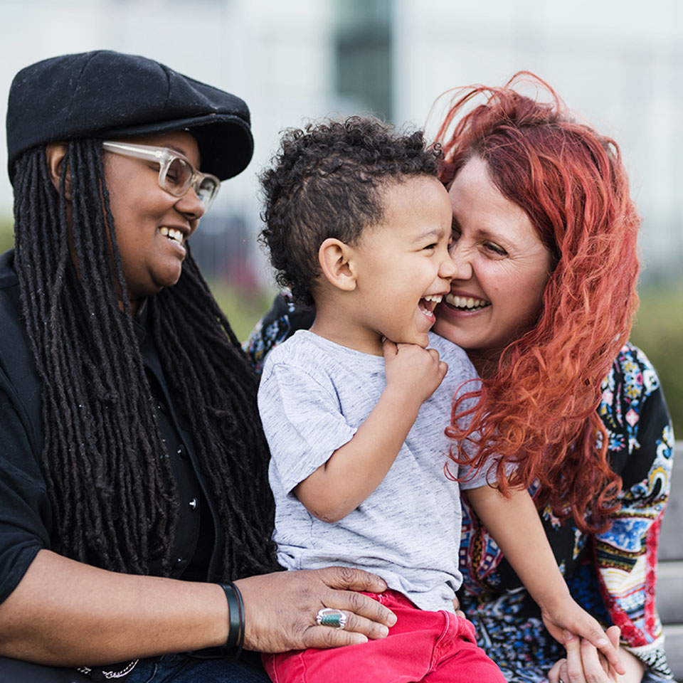 Two mothers holding their son on their laps outside at the park