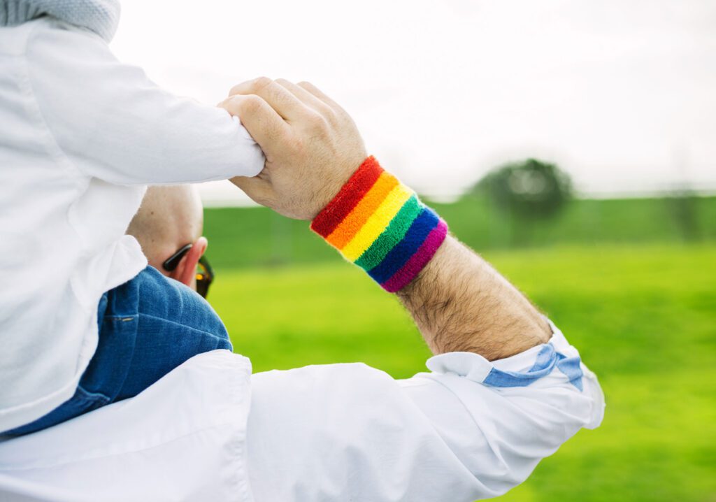 adult with rainbow wristband carries child on shoulders