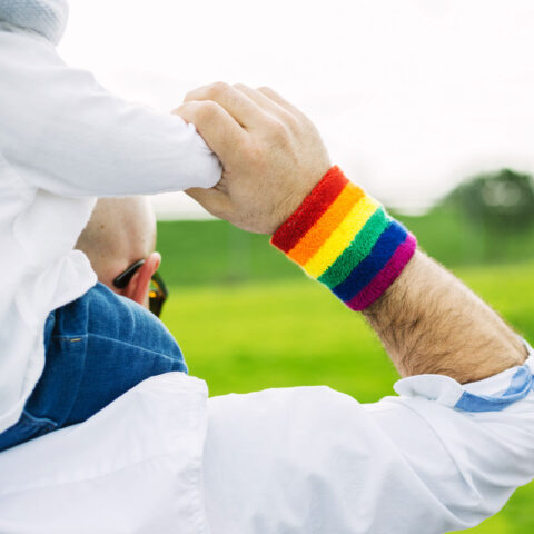 adult with rainbow wristband carries child on shoulders