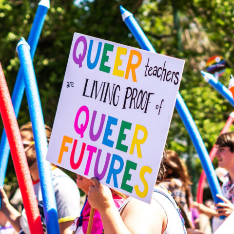 Utah Educators for Pride Group close up of sign  "QUEER teachers are LIVING PROOF of QUEER FUTURES" in the LGBTQIA+ Pride Parade in Salt Lake City, Utah. June 04th, 2023 with multicolored pool noodle pencil props, and flags all unrecognizable.