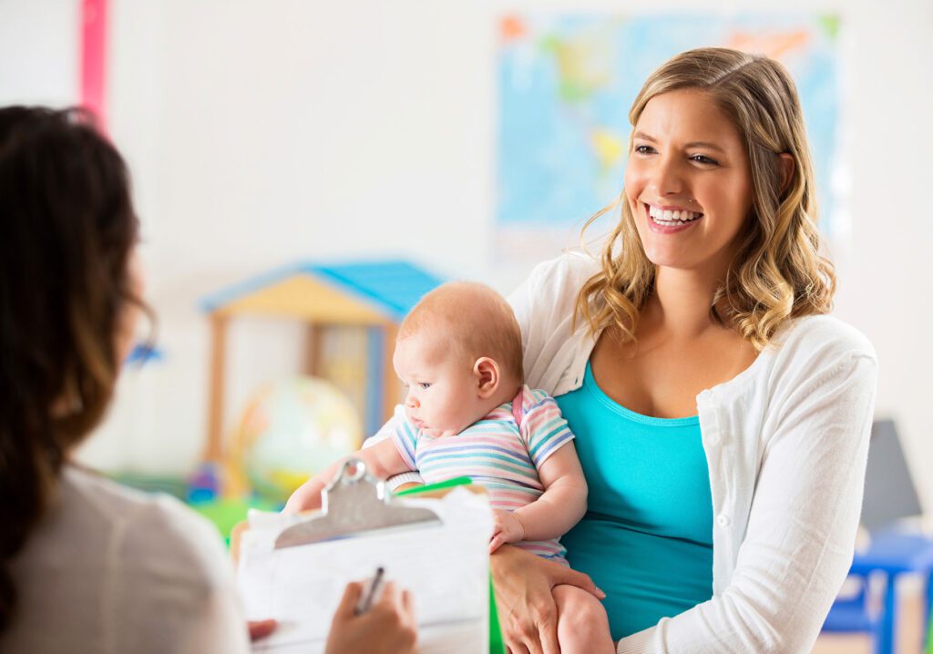 parent speaks to adult with clipboard while holding infant